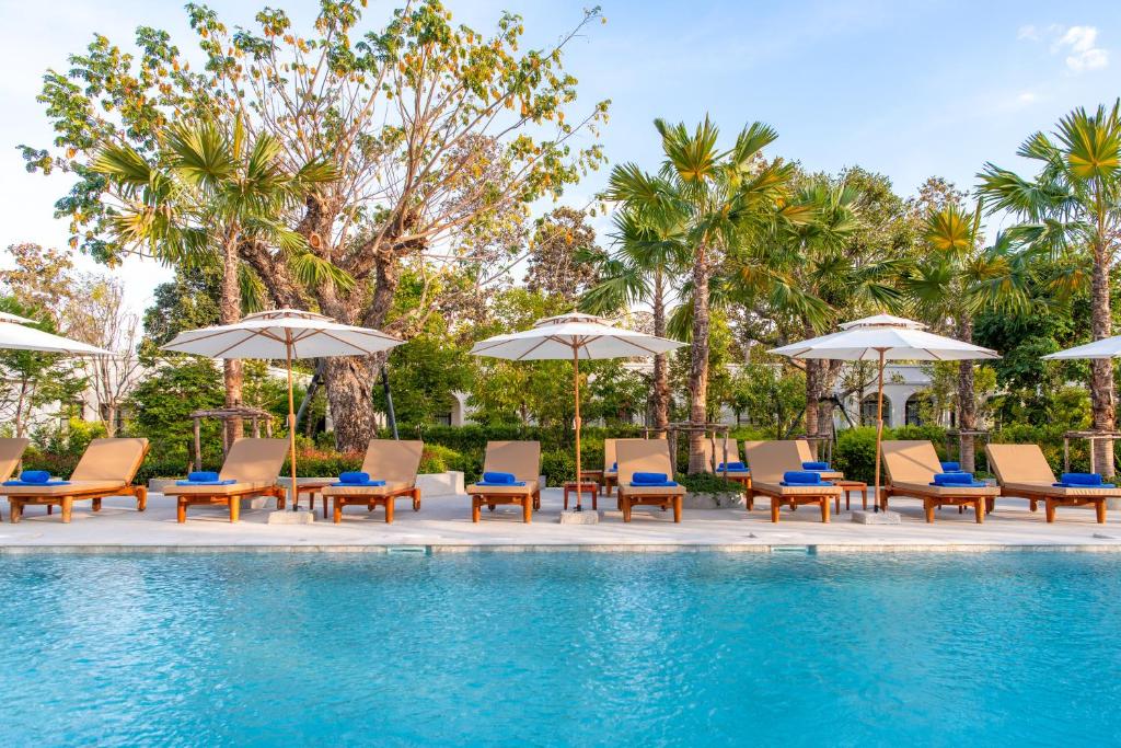 a group of chairs and umbrellas next to a swimming pool at Kaysorn Siri in Ban Kham Kom