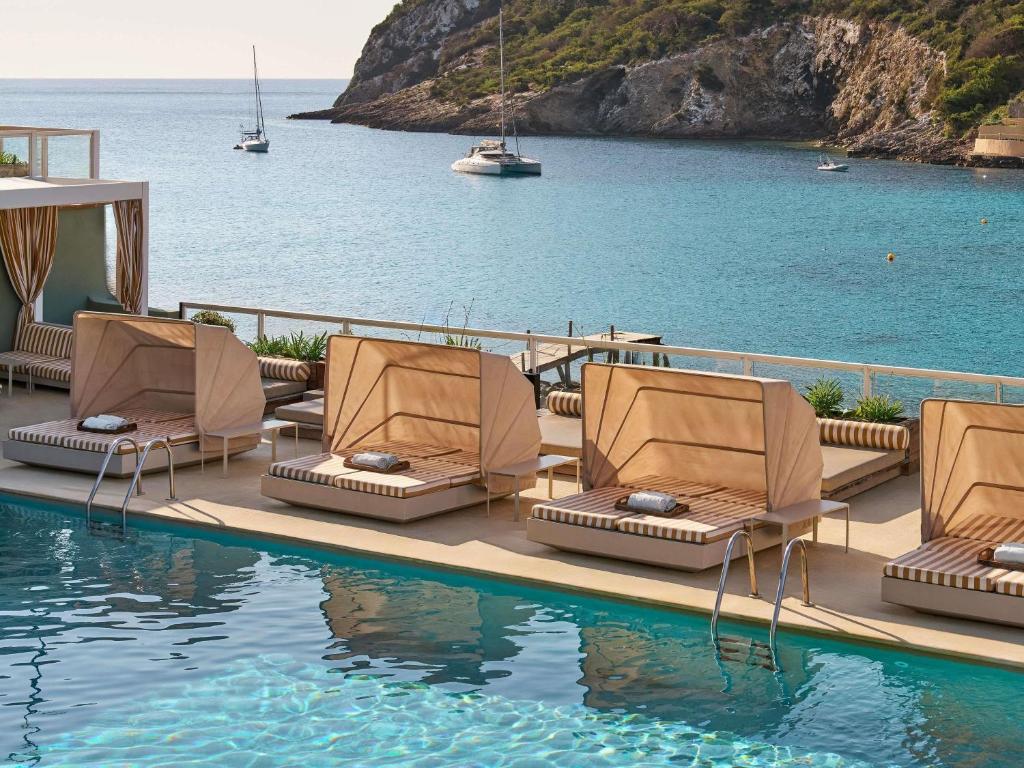 a group of chairs sitting next to a swimming pool at Mondrian Beach Lifestyle Resort By Accor in Cala Llonga