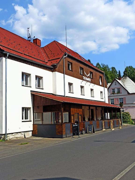 a white building with a red roof on a street at Hotel Schwarz in Nové Hamry