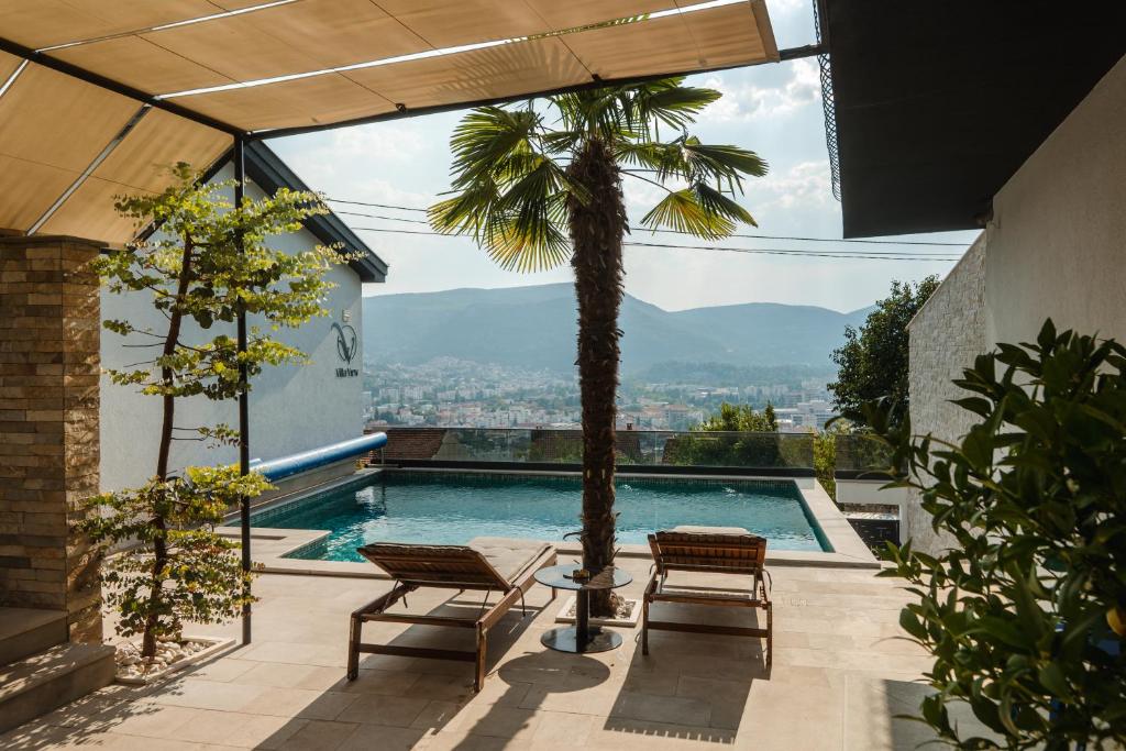 a swimming pool with two chairs and a palm tree at Villa View Mostar with Heated Pool & Jacuzzi in Mostar