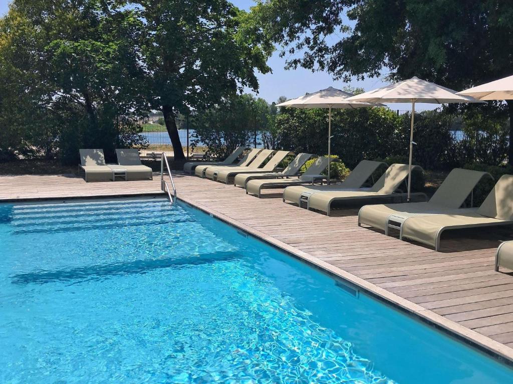 a pool with chaise lounges and umbrellas on a wooden deck at Novotel Bordeaux Lac in Bordeaux