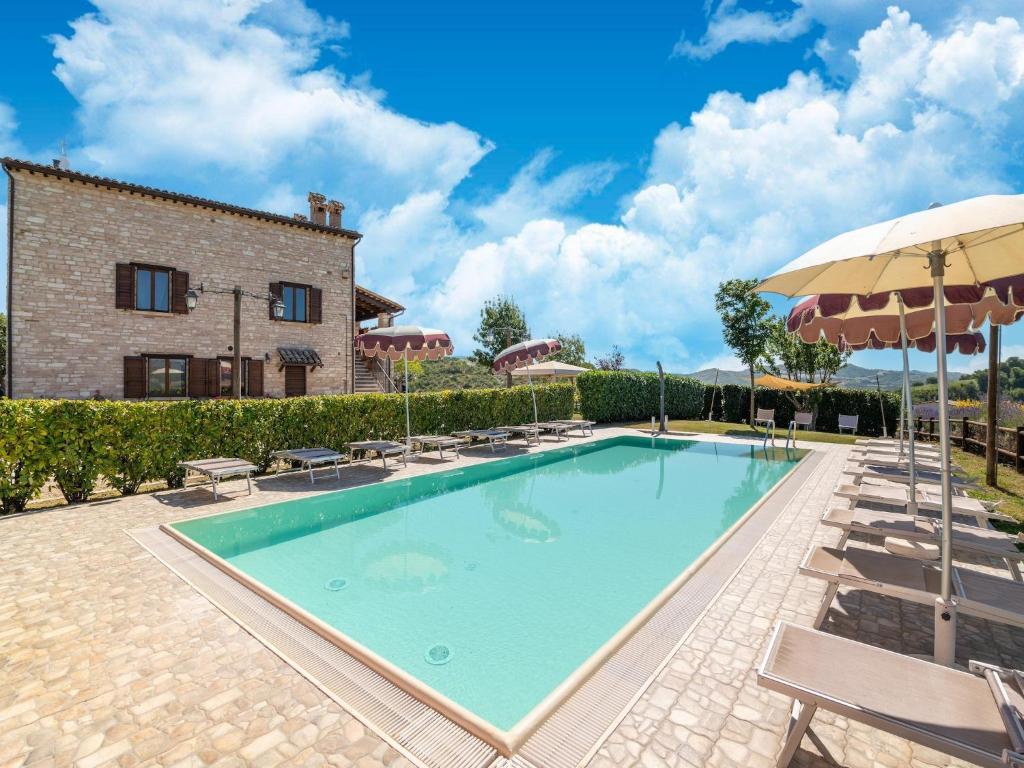 a pool with chairs and an umbrella and a building at Apartment in a farmhouse with 2 swimming pools in Cagli