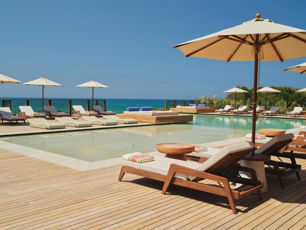 a pool with chairs and umbrellas next to the ocean at Icona's Costa Ragusa Resort - New Opening in Scoglitti