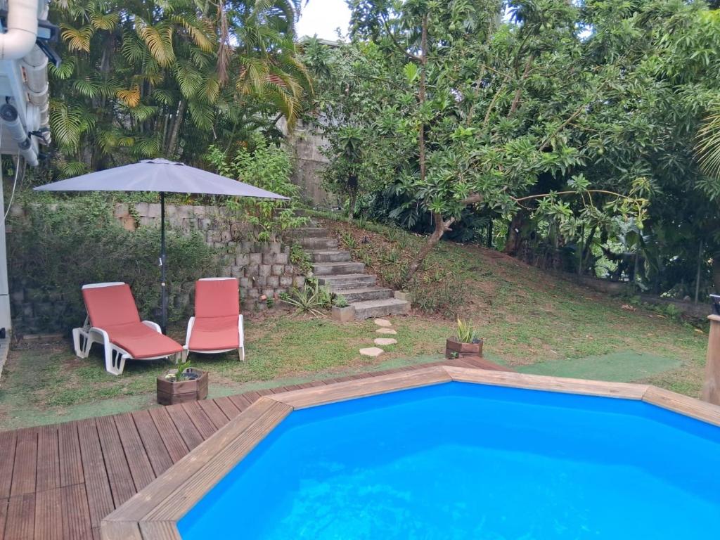 a swimming pool with two chairs and an umbrella at villa Kanel in Le Robert