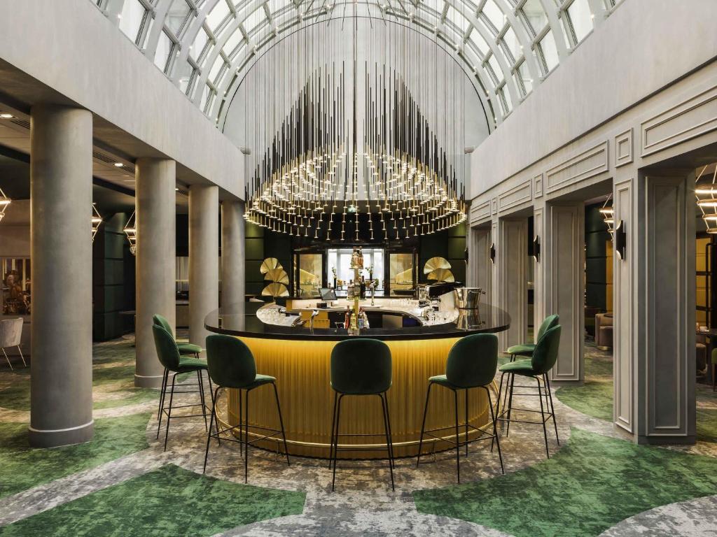 a lobby with a bar with chairs and a chandelier at Le Louis Hotel Versailles Château - MGallery Collection in Versailles