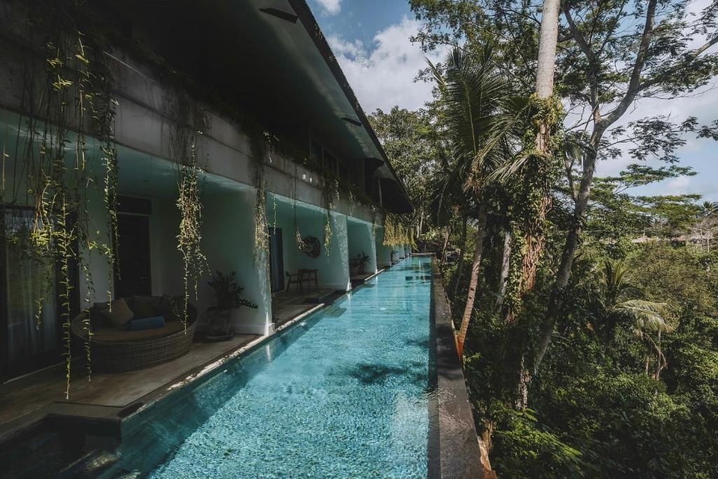 a swimming pool next to a building with trees at The Hidden Paradise Ubud - CHSE Certified in Ubud