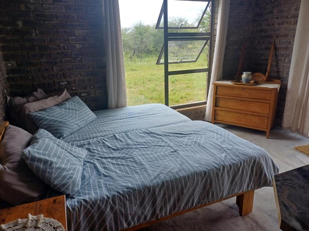 a bed with a blue comforter in a bedroom with a window at BosSpoke Bush Lodge in Thabazimbi