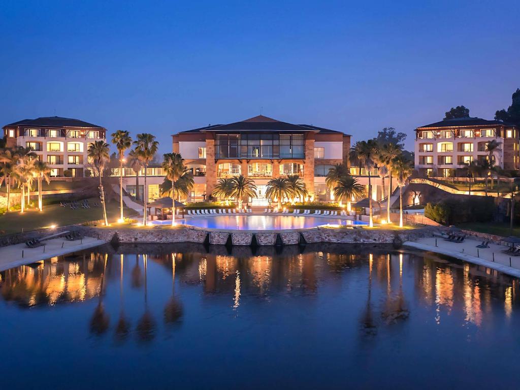 a building with palm trees in front of a body of water at Sofitel La Reserva Cardales in Río Luján