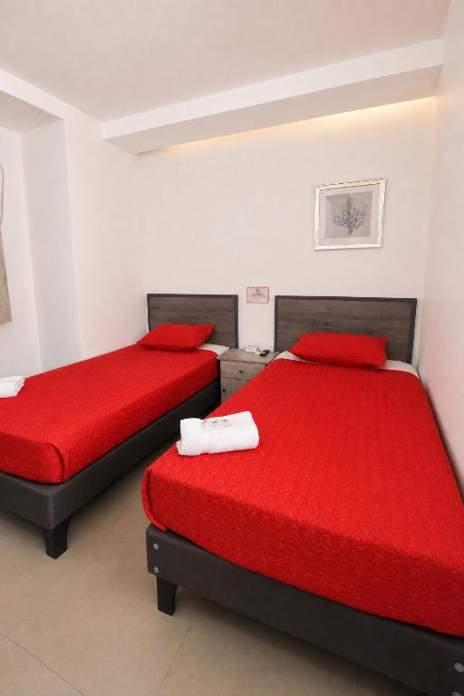 two beds in a room with red sheets and red pillows at Apart Hotel Regata Iquique in Iquique