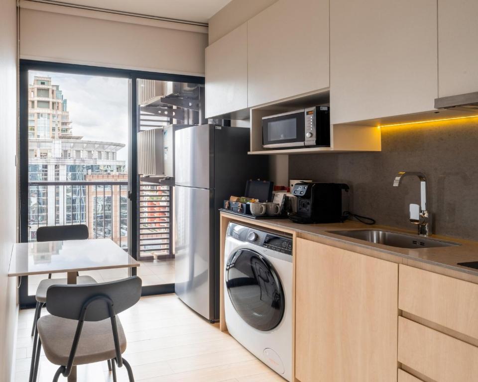 A compact kitchen and laundry area beside a small dining table and city-facing window.
