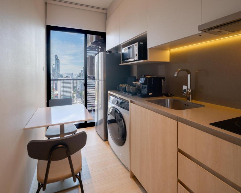 A narrow apartment kitchen with laundry facilities, a two-person table and a city view.