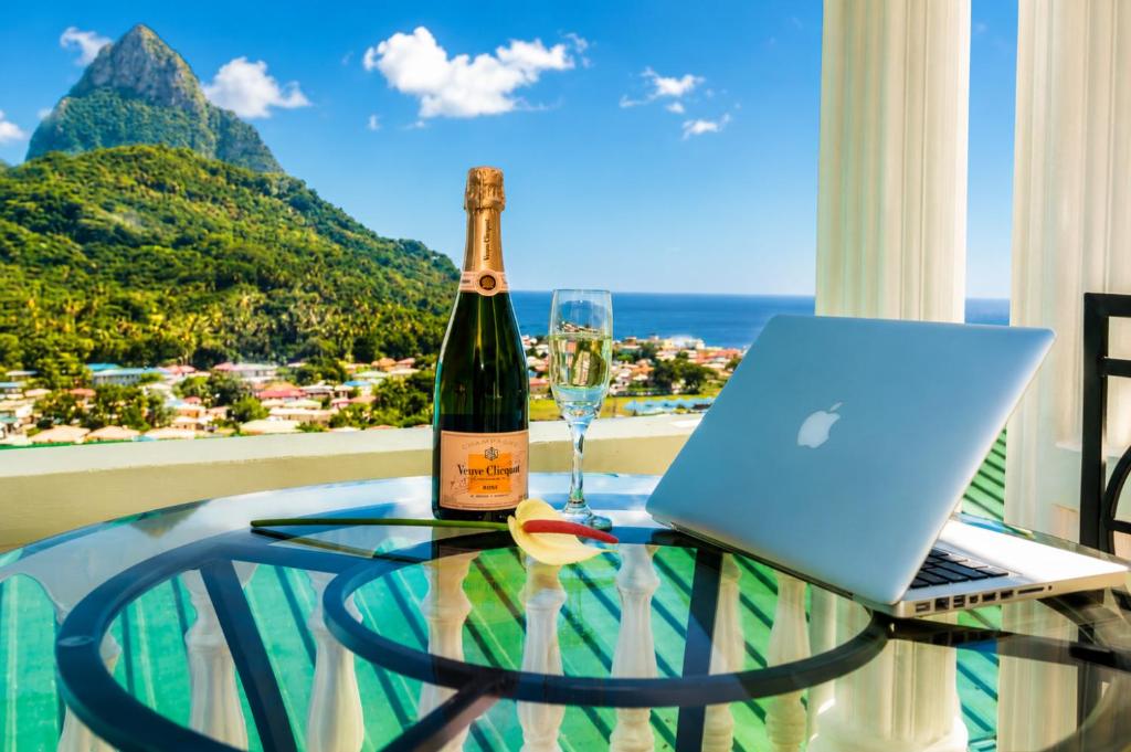 a glass table with a bottle of wine and a laptop at Piton Views & Sunset Balcony, Minutes to Beaches in Soufrière