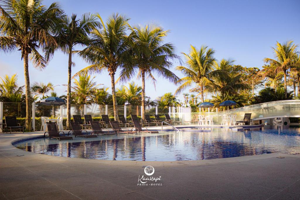 a swimming pool with chairs and palm trees at Kaakupe Praia Hotel in Guaratuba