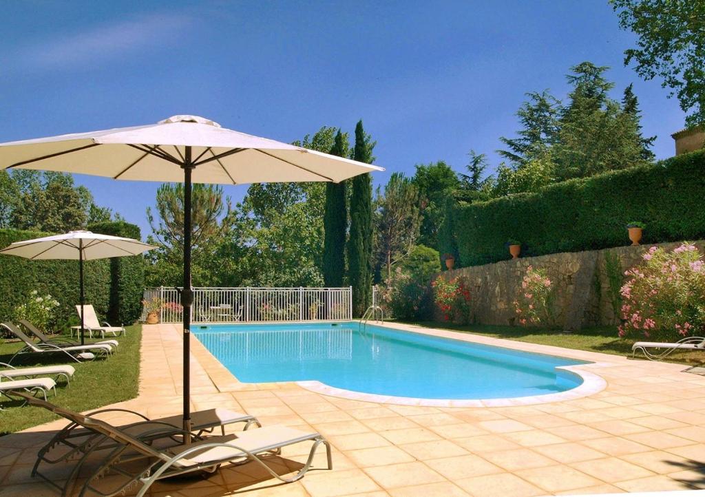a swimming pool with an umbrella and two chairs and a table at Bastide le Luget in Vénéjan