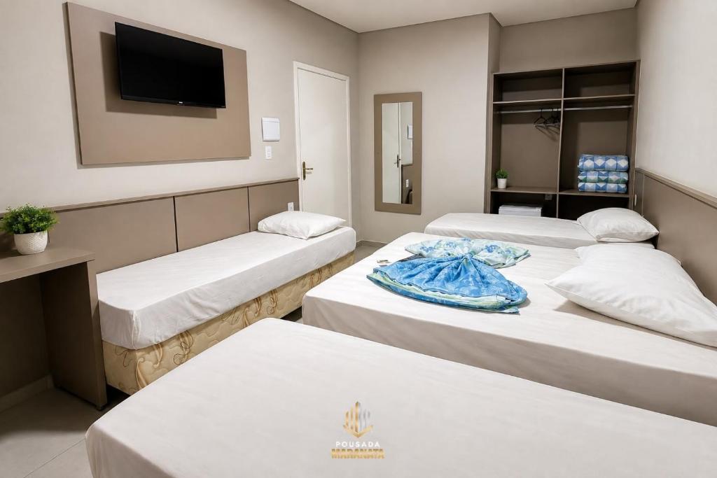 a hotel room with three beds and a television at Pousada Maranata in Aparecida