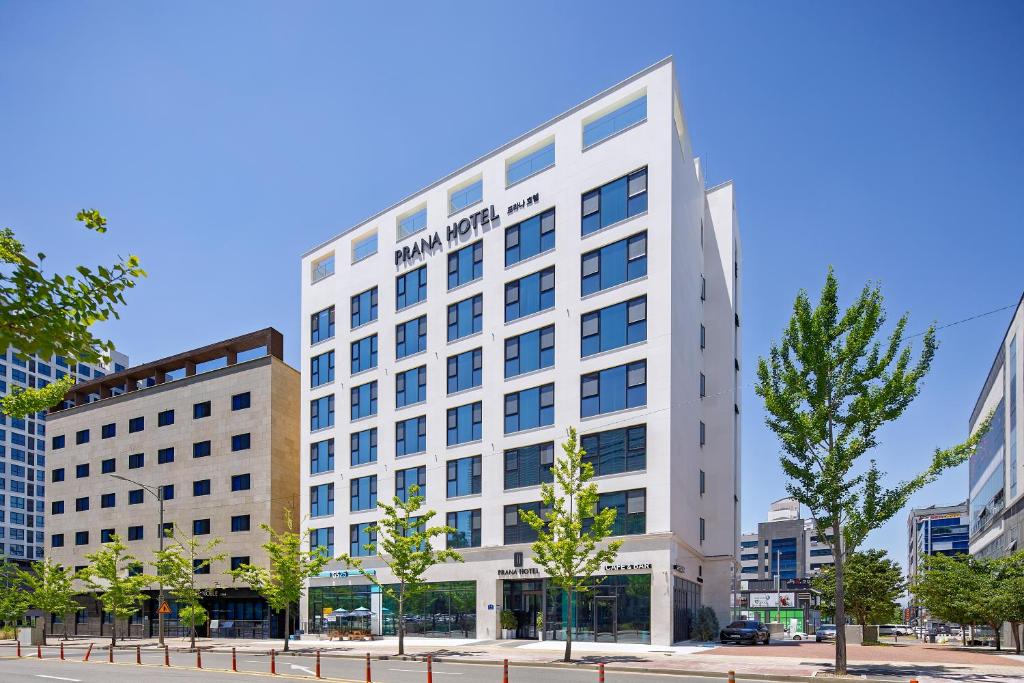 a large white building in a city with trees at Daegu Hyeonpung Prana Hotel in Daegu