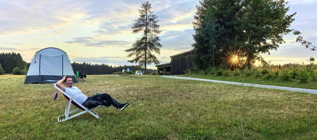 a man laying in a lawn chair next to a tent at Almplatz mit Weitblick in Langschlag
