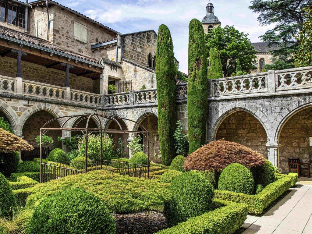 a garden with bushes and trees in front of a building at Mercure Figeac Viguier du Roy in Figeac