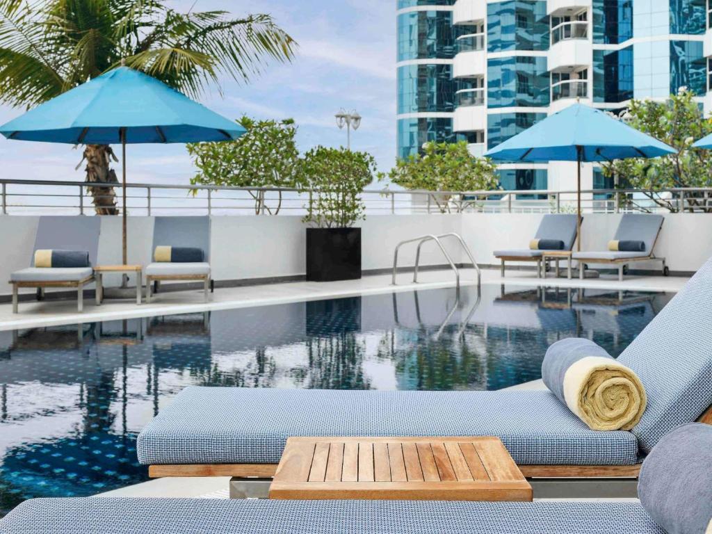 a pool with chairs and umbrellas on a building at Mövenpick Hotel Jumeirah Lakes Towers Dubai in Dubai