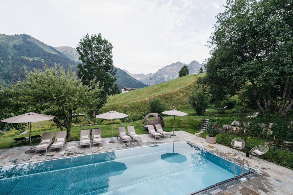a swimming pool with chairs and umbrellas at Das Naturhotel Chesa Valisa in Hirschegg