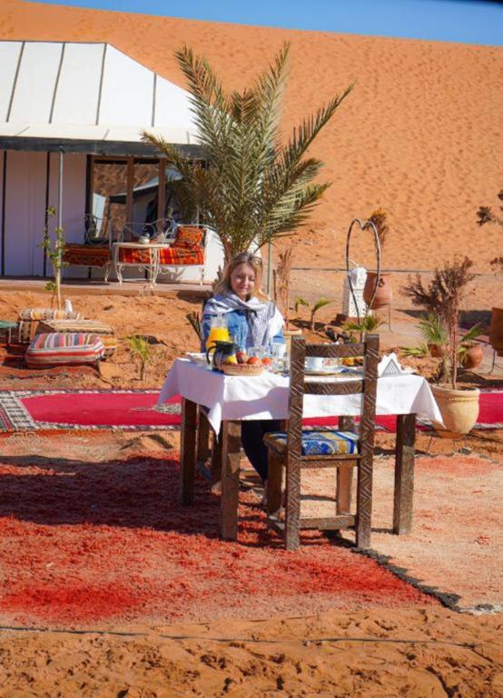 a woman sitting at a table in the desert at Camel Trekking Camp & Activities in Merzouga