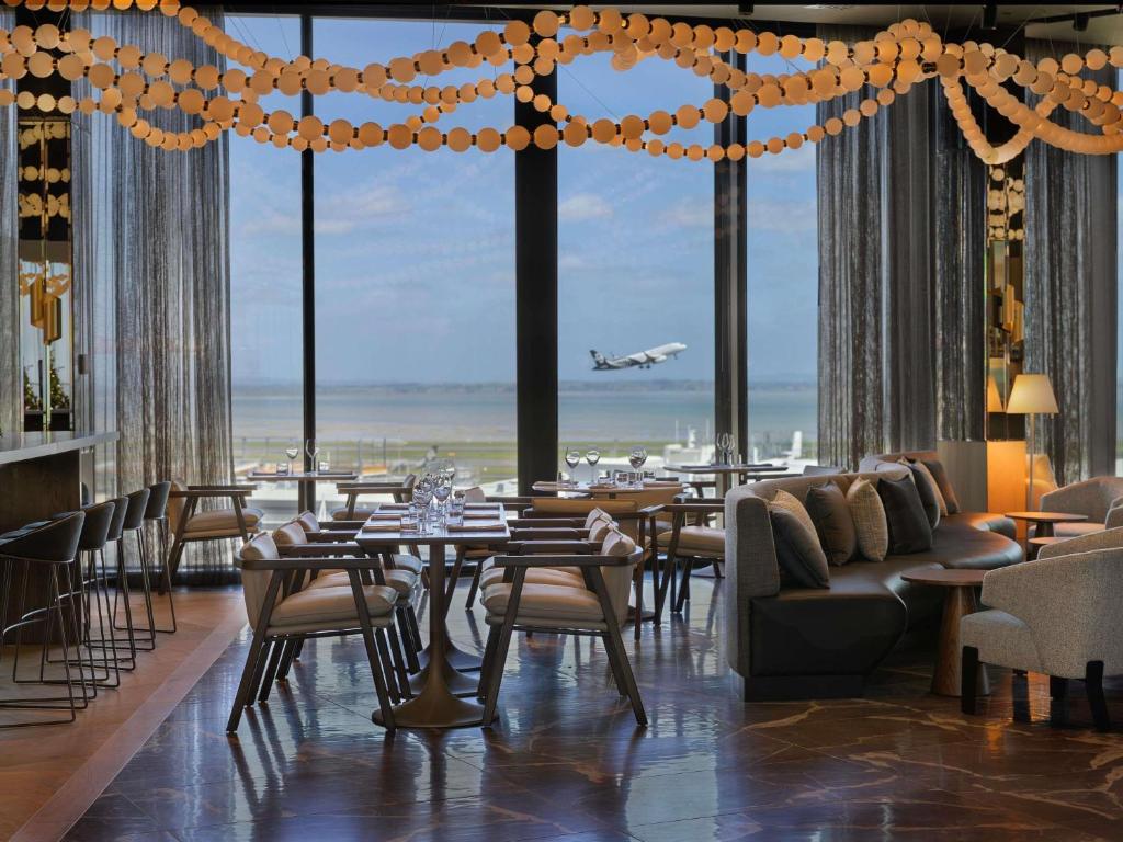 a restaurant with tables and chairs and an airplane taking off at Pullman Auckland Airport in Auckland