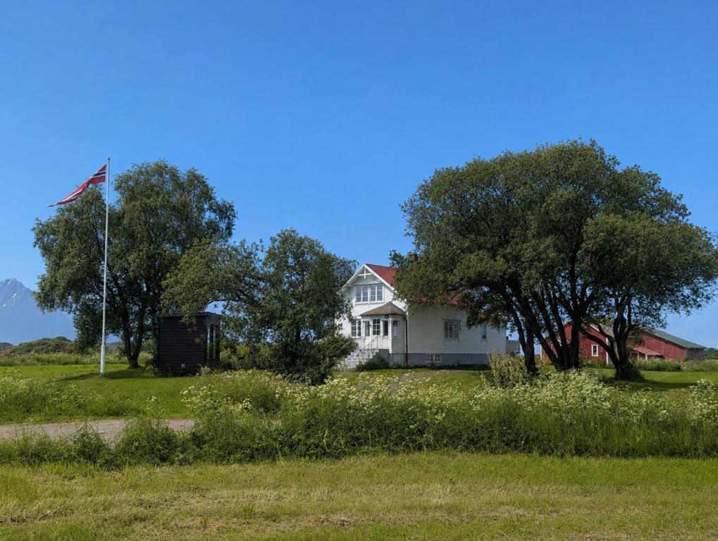 a white house with an american flag in a field at Borghildstua Feriehus Romslig feriehus med panoramautsikt mot havet og Lofotfjellene in Melbu