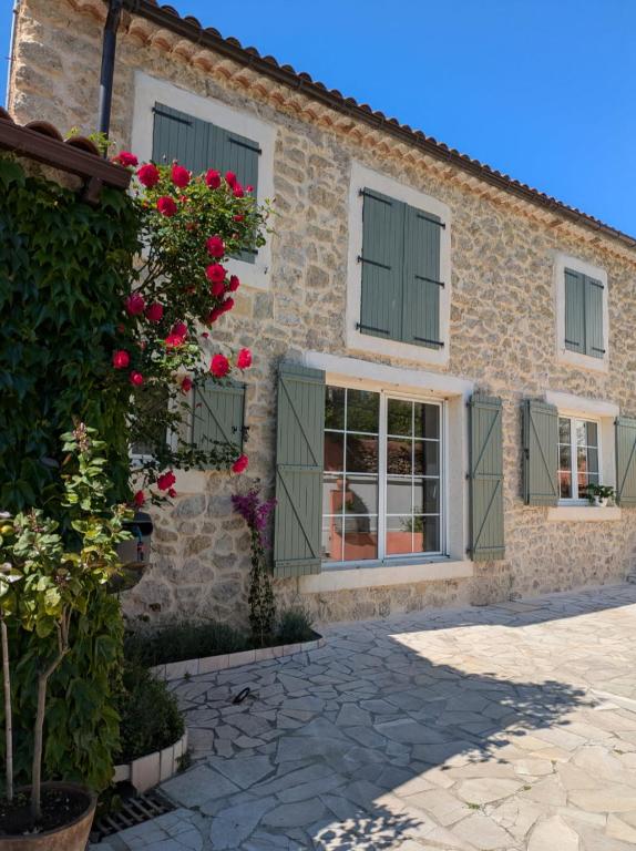 a stone house with green windows and roses at Aux Berges du Canal in Capestang