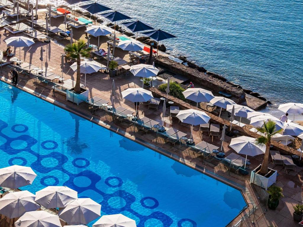 an overhead view of a swimming pool with umbrellas and the ocean at Pullman Cannes Mandelieu in Mandelieu-La Napoule