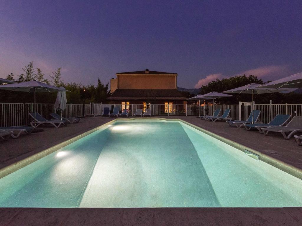 a swimming pool at night with chairs and umbrellas at ibis Sisteron in Sisteron
