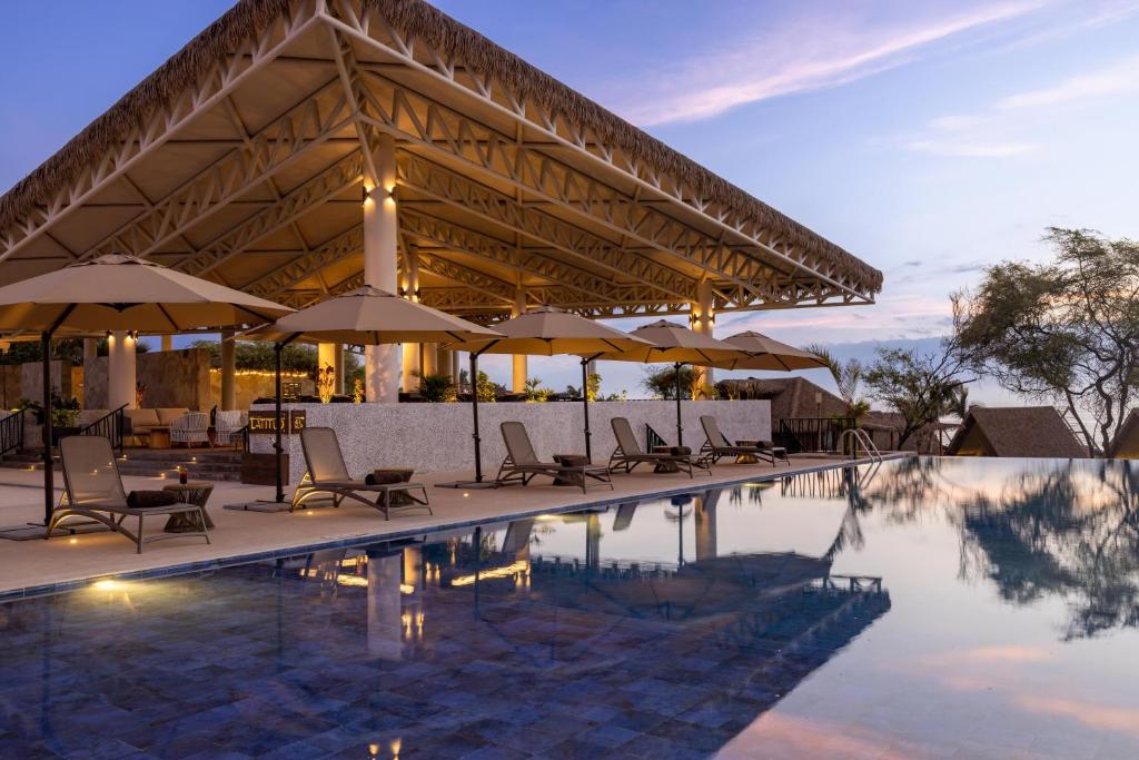 a pool with chairs and umbrellas next to a building at Aranwa Vichayito Beach Resort in Vichayito