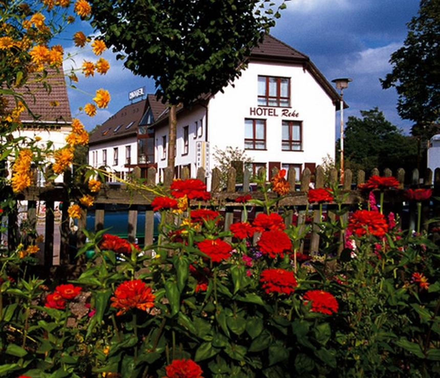 a white building with red flowers in front of a fence at Hotel Reke in Plau am See