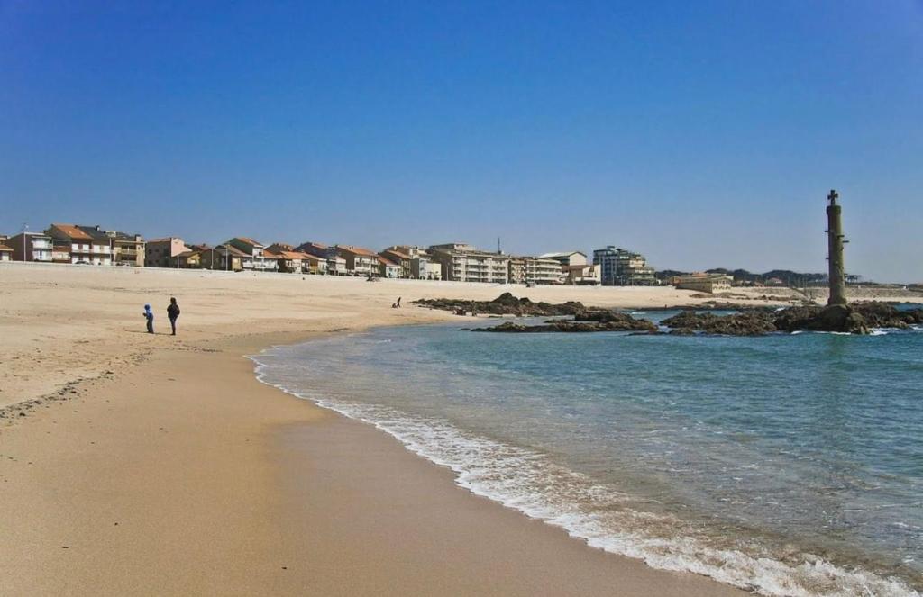 two people walking on a beach near the water at Casa Dourado Ramos in Vila do Conde