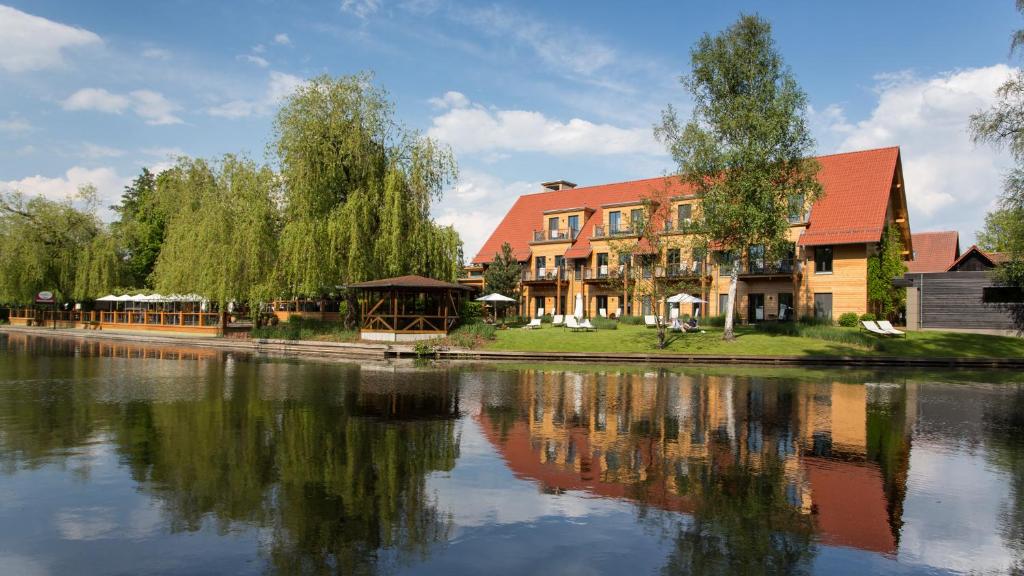 um edifício ao lado de um corpo de água com árvores em Hotel Strandhaus - Boutique Resort & Spa em Lübben