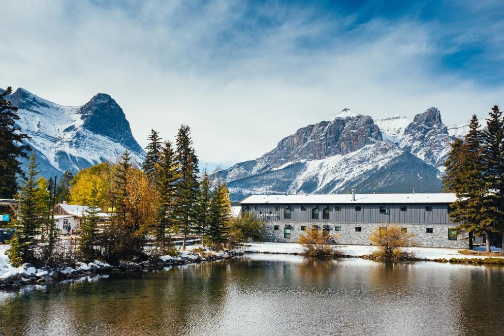a building next to a lake with snowy mountains at Lamphouse By Basecamp in Canmore