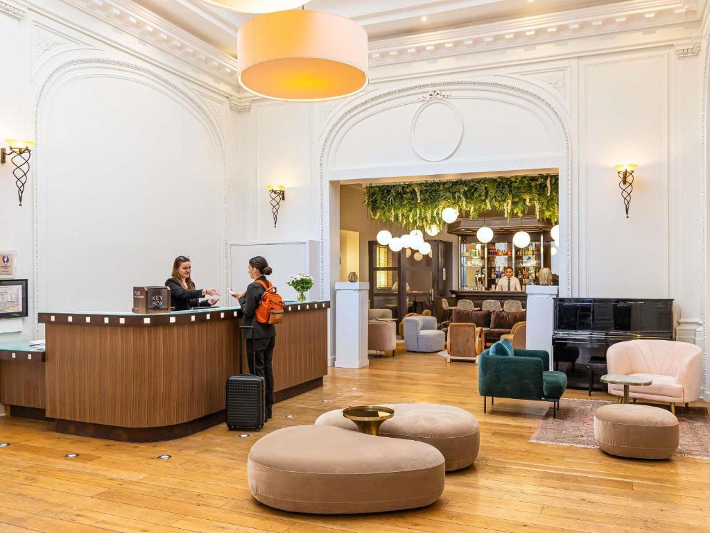 a woman standing at a counter in a hotel lobby at Mercure Lille Roubaix Grand Hôtel in Roubaix