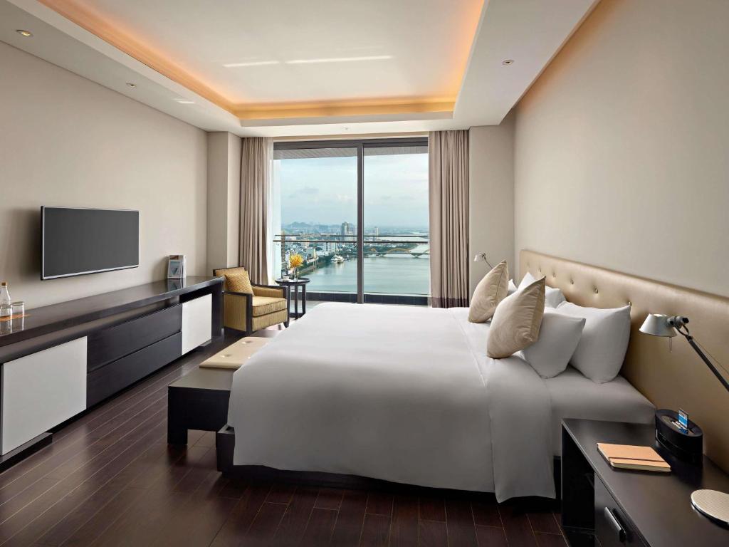 A king-bed room with a floor-to-ceiling window overlooking the water and city.