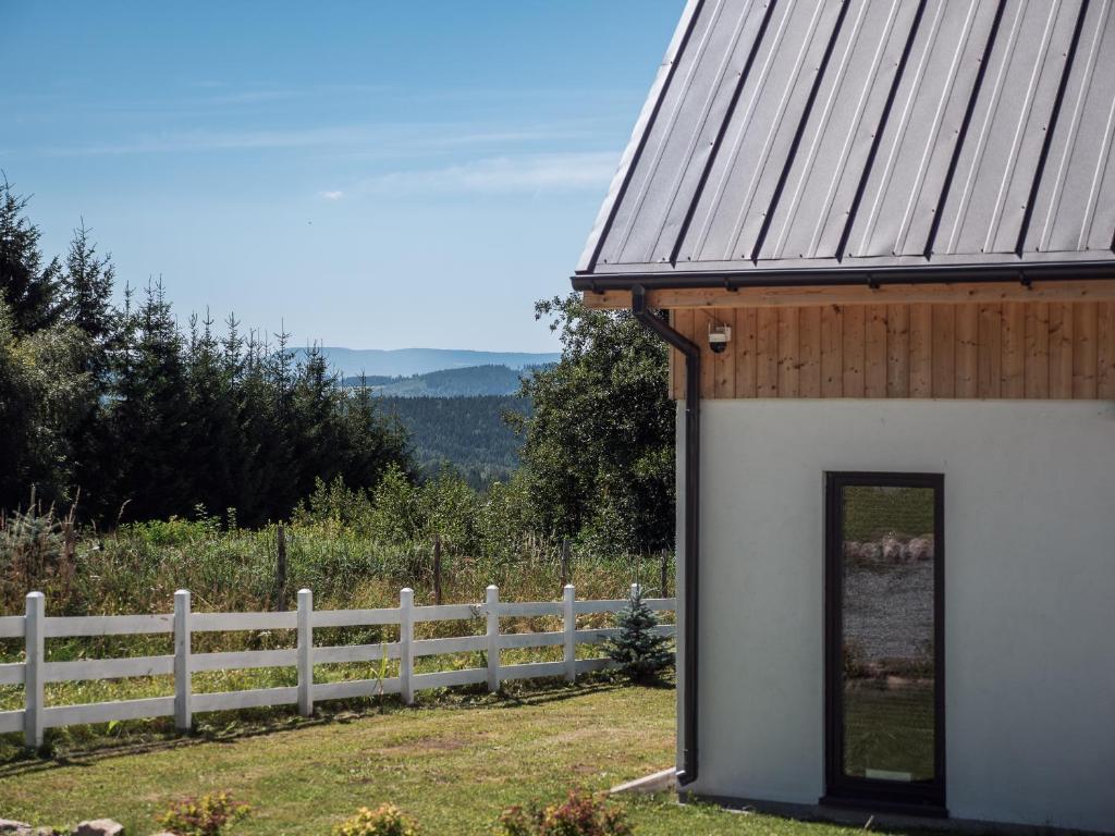 a white building with a wooden roof next to a fence at SierPlejs Hill - domki przy szlaku w Górach Sowich in Sierpnica