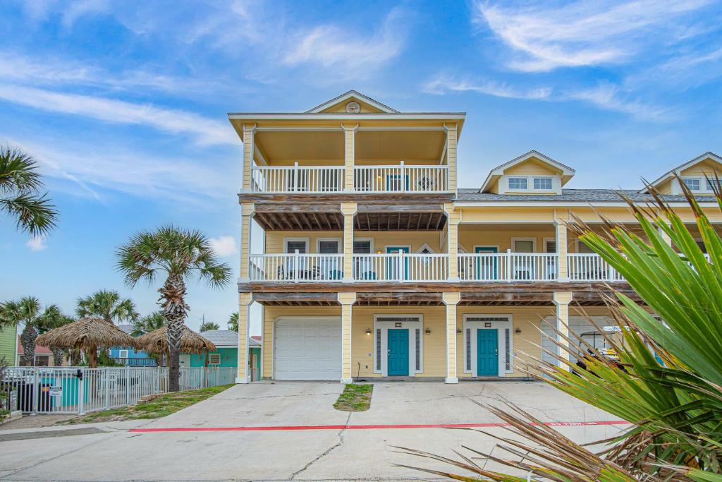 a large yellow house with a balcony and palm trees at Sandbar in Port Aransas