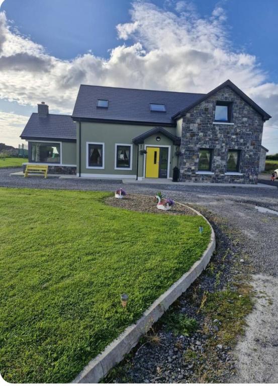 a house with a yellow door and a grass yard at Double room with ensuite in Milltown Malbay
