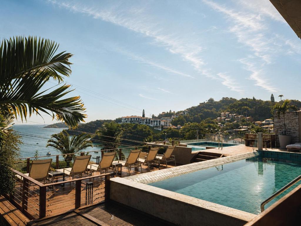a swimming pool with chairs and a view of the water at HOTEL VILLE LA PLAGE & BEACH CLUB in Búzios