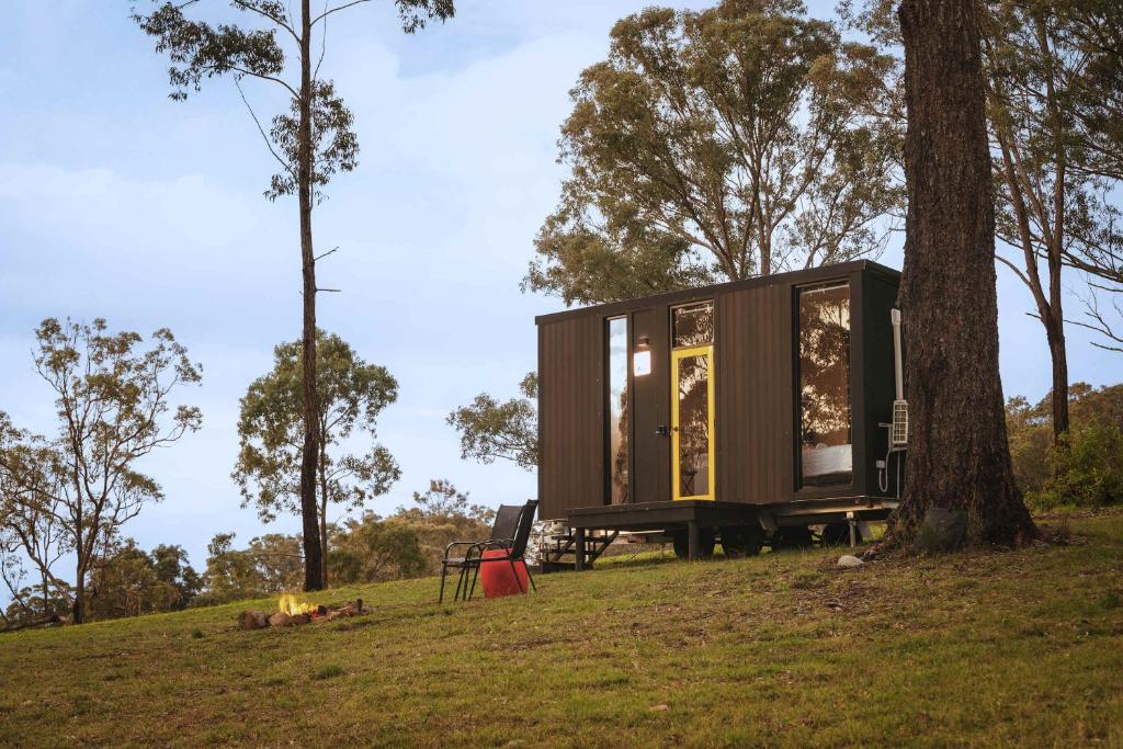 a tiny house sitting on a hill next to a tree at Three-Kalm & Four-Sol by Tiny Away in Rainbow Flat