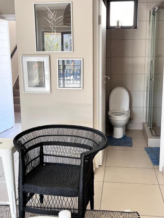 a bathroom with a toilet and a black wicker chair at Modern Heritage Condo in Fourways