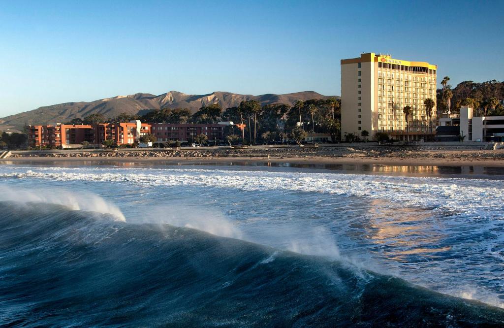 a wave in the water on a beach with buildings at Crowne Plaza Ventura Beach by IHG in Ventura