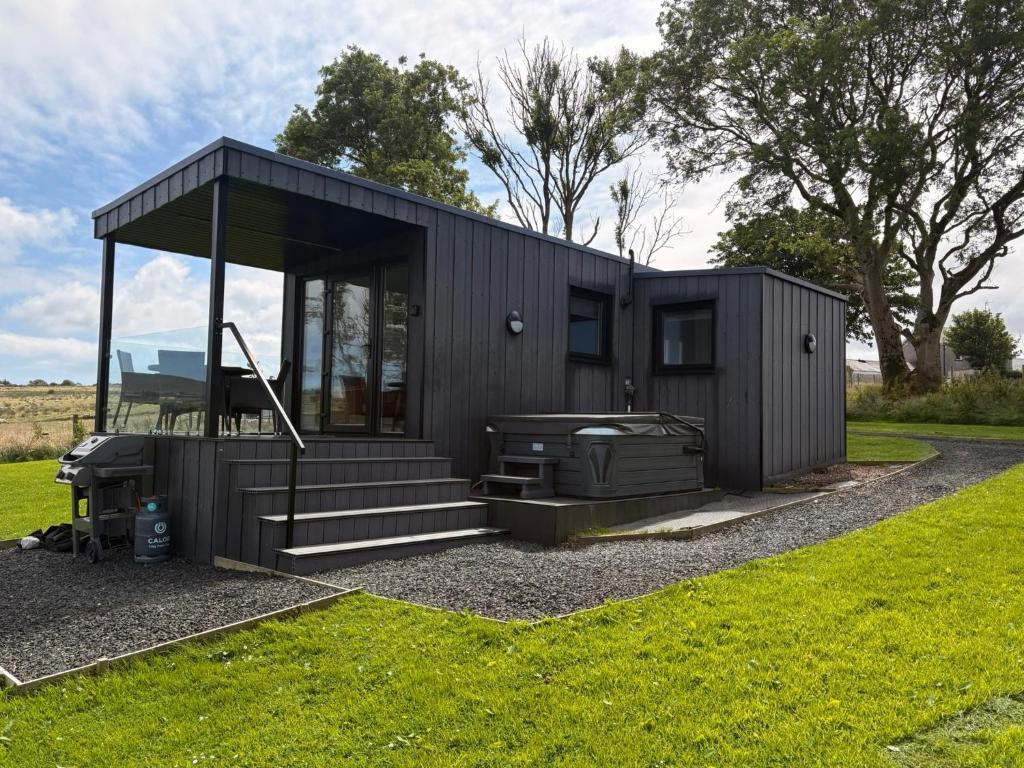 a black tiny house with a grill in a yard at Luxury Glamping Cabin sleeping 4 People with Private Hot Tub and BBQ with views across the North Coast Ballycastle Pod 2 in Ballycastle
