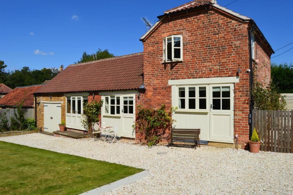 una casa de ladrillo con puertas blancas y un banco en The Coach House Denton, en Grantham