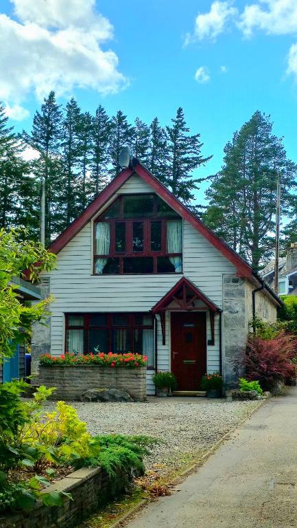 a white house with a red door and flowers at The Old Stables in Fort Augustus