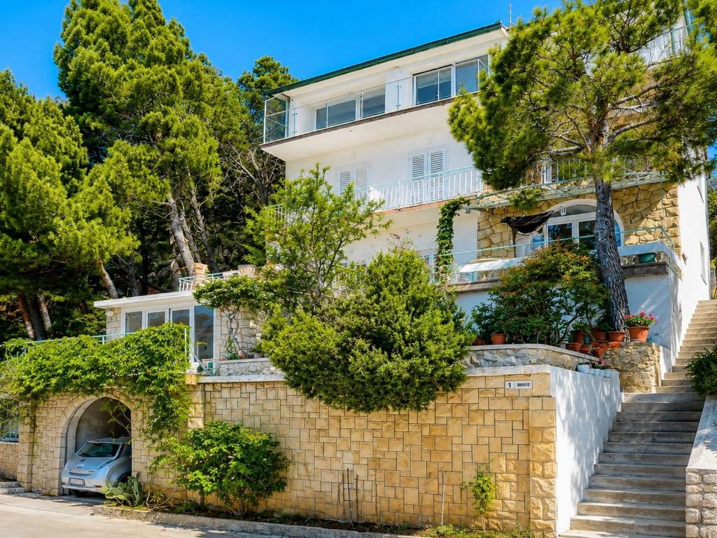 a house with a stone wall and trees at Rooms Jakirusa in Brela