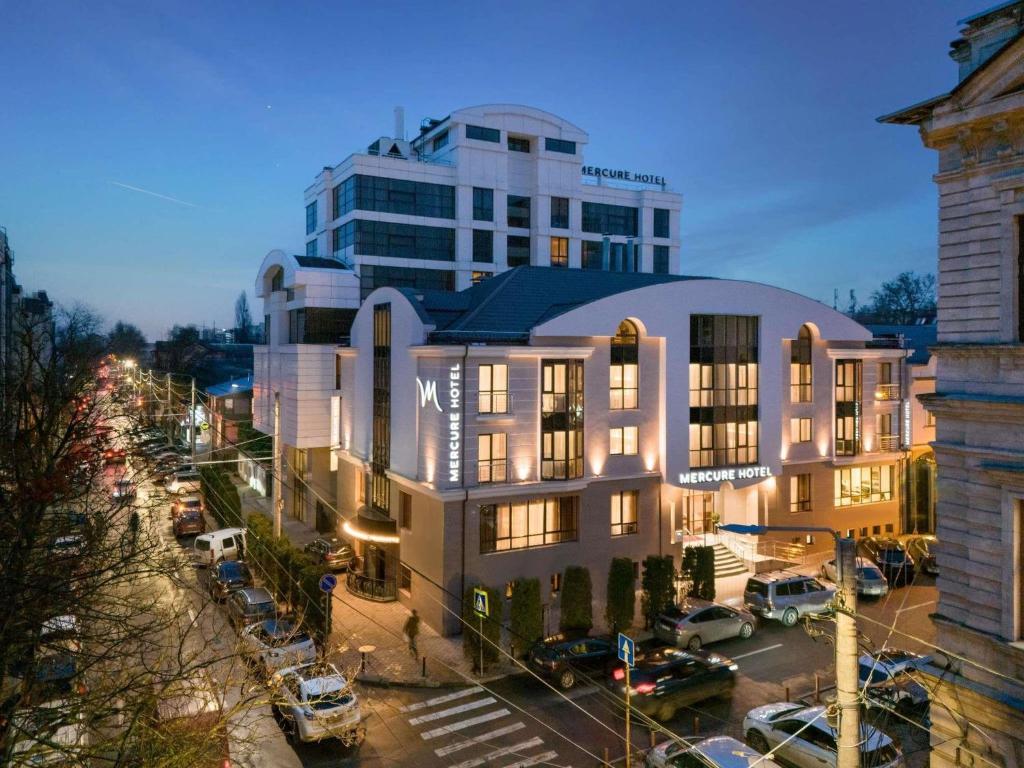 a building with a lot of cars parked in a parking lot at Mercure Chisinau Center Jazz Hotel in Chişinău