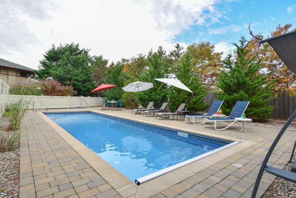 a swimming pool with chairs and umbrellas in a yard at Beautiful backyard pool deeded beach rights in Truro